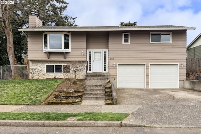 bi-level home featuring fence, an attached garage, a chimney, concrete driveway, and a front lawn