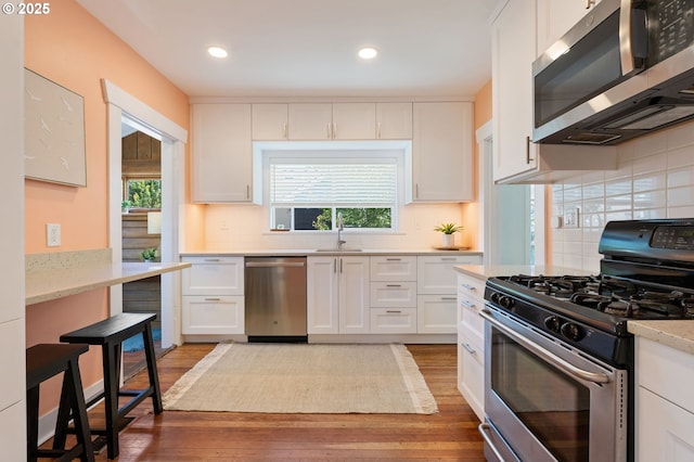 9935 N Lombard St, Portland, OR 97203 - kitchen featuring stainless steel appliances, a sink, white cabinets, light wood finished floors, and decorative backsplash