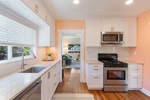 9935 N Lombard St, Portland, OR 97203 - kitchen featuring appliances with stainless steel finishes, a sink, wood finished floors, white cabinets, and decorative backsplash