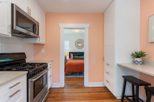 9935 N Lombard St, Portland, OR 97203 - kitchen with appliances with stainless steel finishes, light wood-style flooring, tasteful backsplash, and white cabinets