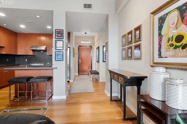 kitchen with a breakfast bar, decorative backsplash, and light hardwood / wood-style flooring