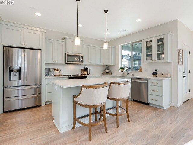 kitchen with appliances with stainless steel finishes, decorative light fixtures, white cabinetry, a center island, and light wood-type flooring