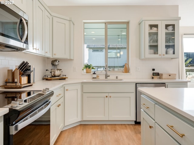 kitchen featuring sink, white cabinetry, light wood-type flooring, appliances with stainless steel finishes, and decorative backsplash