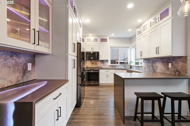 kitchen featuring white cabinetry, a peninsula, dark wood-type flooring, and stainless steel appliances