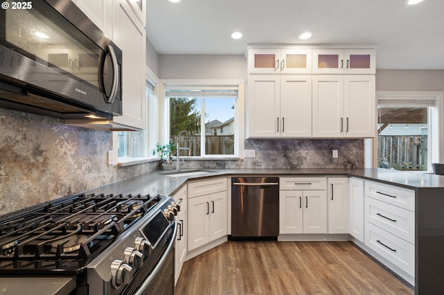 kitchen with a sink, stainless steel appliances, white cabinets, light wood-style floors, and dark countertops