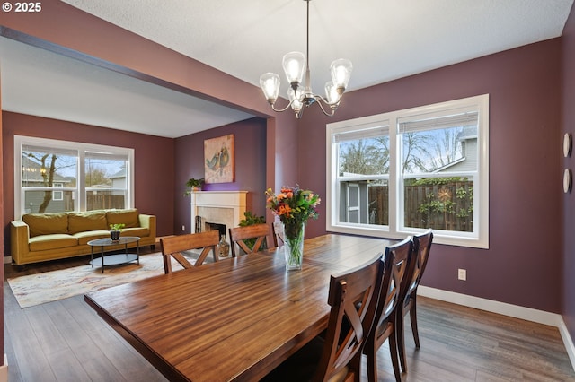 dining area with wood finished floors, a fireplace, baseboards, and a chandelier