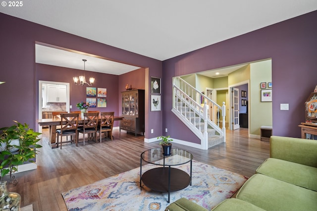 living room featuring a notable chandelier, stairway, baseboards, and wood finished floors