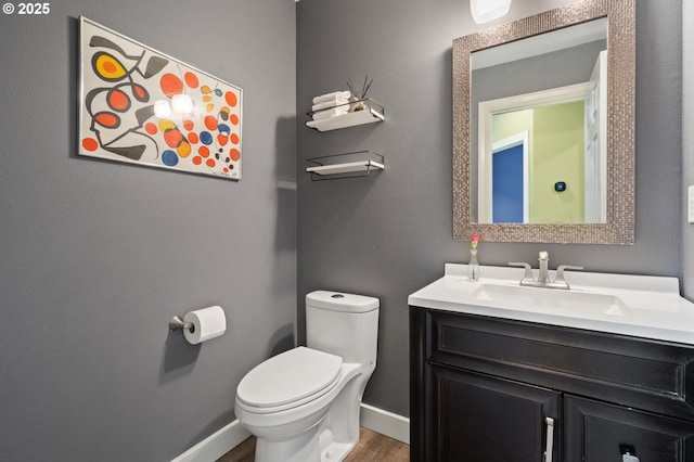 half bath with vanity, toilet, wood finished floors, and baseboards