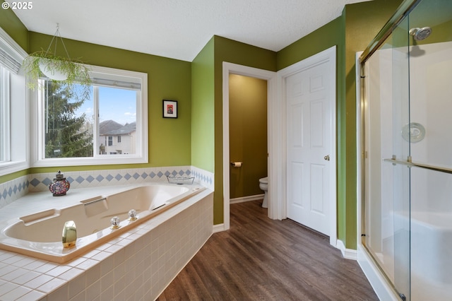 full bath featuring wood finished floors, a garden tub, a stall shower, and toilet