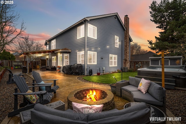 back of house at dusk with a patio, fence, an outdoor living space with a fire pit, and a hot tub