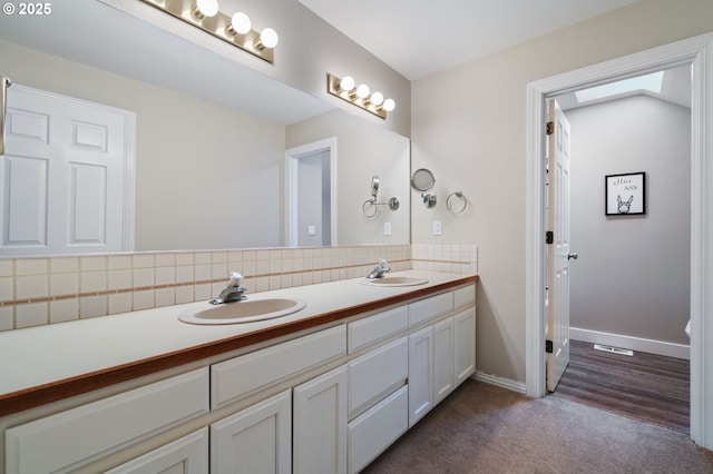 bathroom featuring double vanity, decorative backsplash, baseboards, and a sink