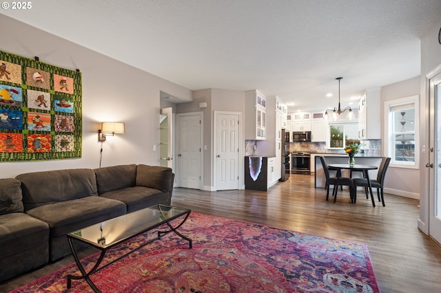 living room with baseboards, an inviting chandelier, and dark wood-style flooring