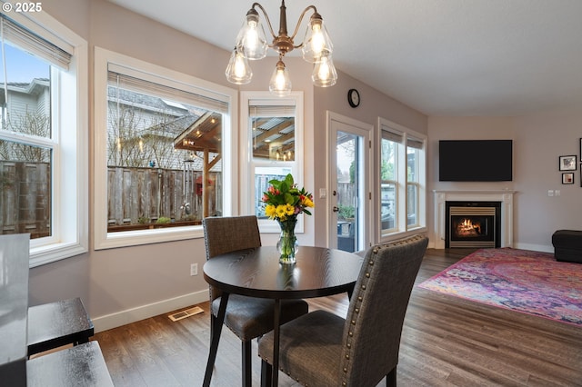 dining area featuring a lit fireplace, visible vents, baseboards, and wood finished floors