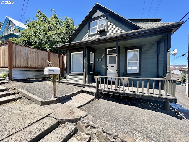 bungalow-style house with covered porch, a shingled roof, cooling unit, and fence