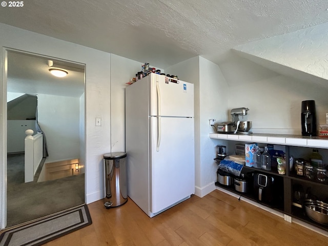 kitchen with baseboards, wood finished floors, freestanding refrigerator, vaulted ceiling, and a textured ceiling