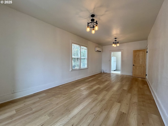 spare room with baseboards, a wall unit AC, a notable chandelier, and light wood finished floors