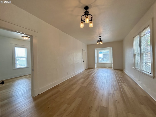 unfurnished dining area with baseboards, a notable chandelier, a wealth of natural light, and light wood-style floors