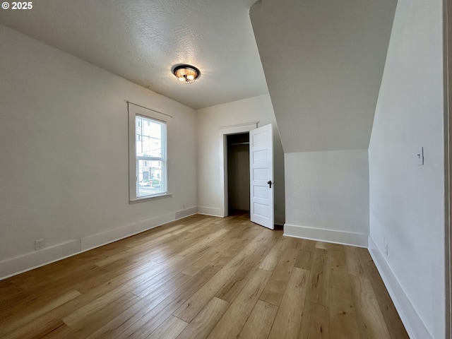 unfurnished bedroom featuring a closet, baseboards, a textured ceiling, and light wood finished floors