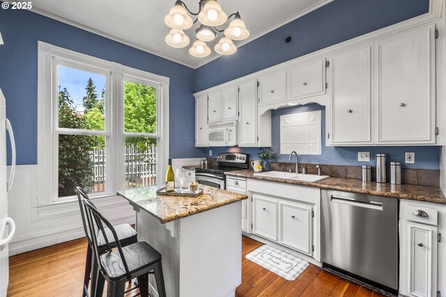 1067 Oak St, Silverton, OR 97381 - kitchen featuring appliances with stainless steel finishes, a sink, a chandelier, white cabinetry, and hardwood / wood-style floors