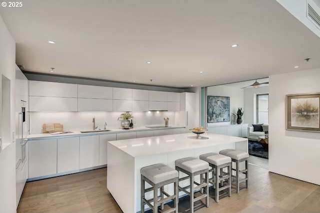 kitchen with modern cabinets, a sink, a breakfast bar, white cabinetry, and recessed lighting