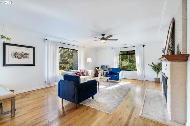 living room with light wood finished floors, a fireplace, baseboards, and a ceiling fan