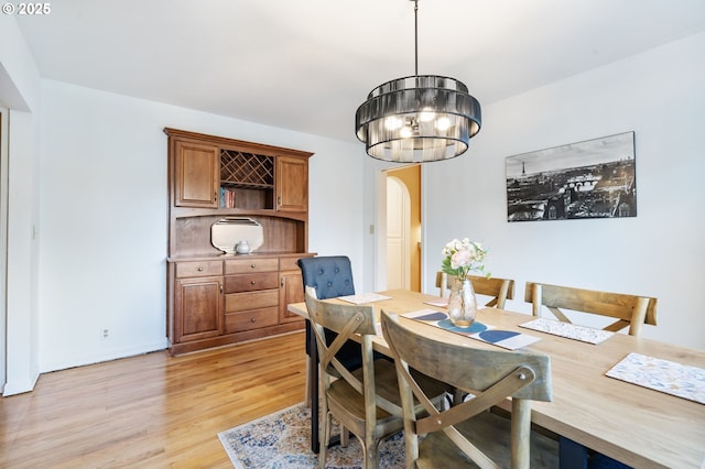 dining space with light wood finished floors, arched walkways, and a notable chandelier