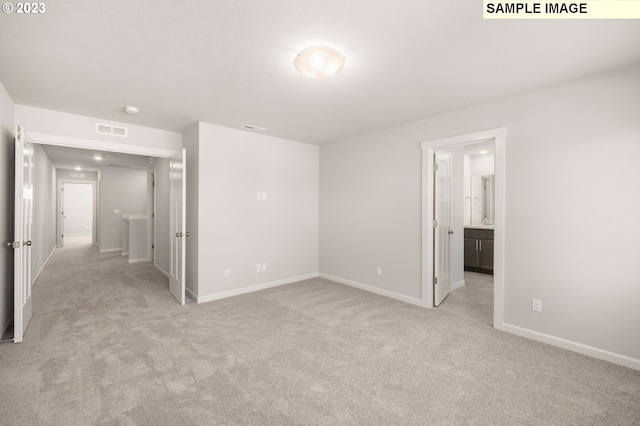 unfurnished bedroom with light carpet, ensuite bath, visible vents, and baseboards