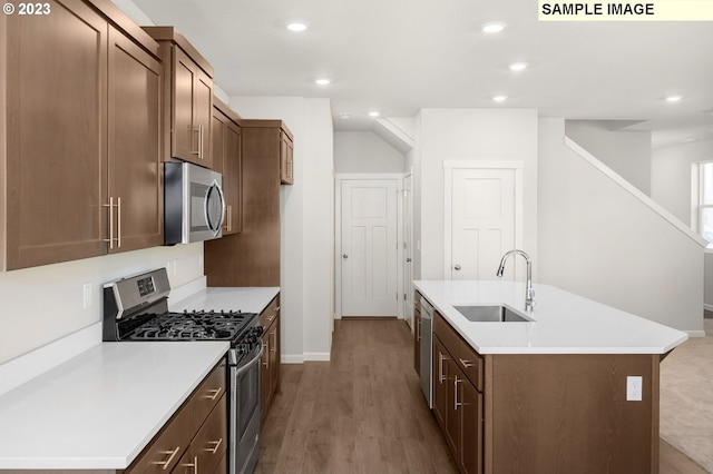 kitchen with an island with sink, wood finished floors, light countertops, stainless steel appliances, and a sink