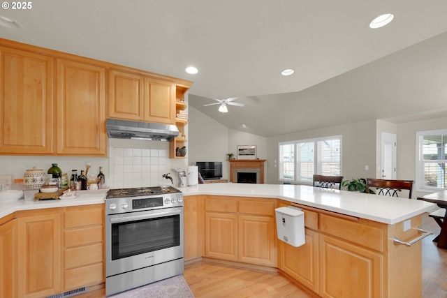 kitchen with light countertops, light brown cabinetry, stainless steel gas stove, a peninsula, and under cabinet range hood