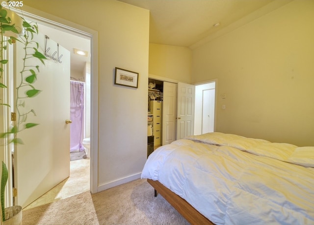 bedroom featuring light carpet, lofted ceiling, ensuite bathroom, and a closet