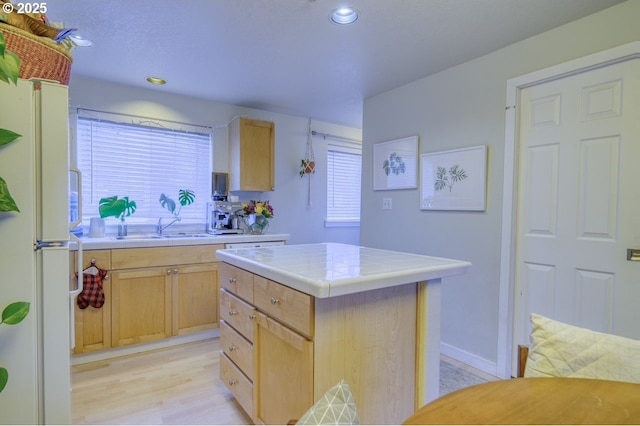 kitchen featuring tile countertops, white refrigerator, a center island, light brown cabinets, and sink