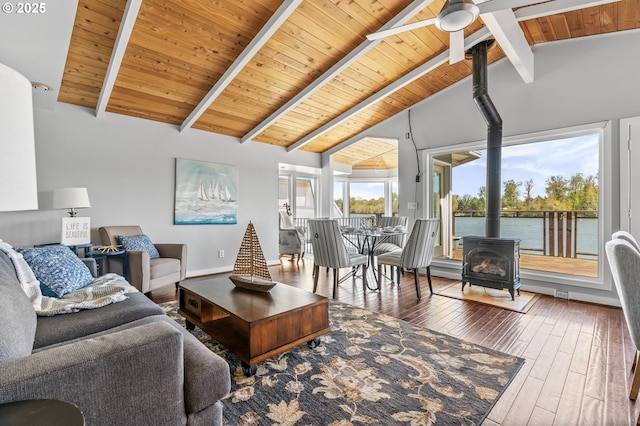 living room featuring ceiling fan, a wood stove, hardwood / wood-style floors, beamed ceiling, and wood ceiling