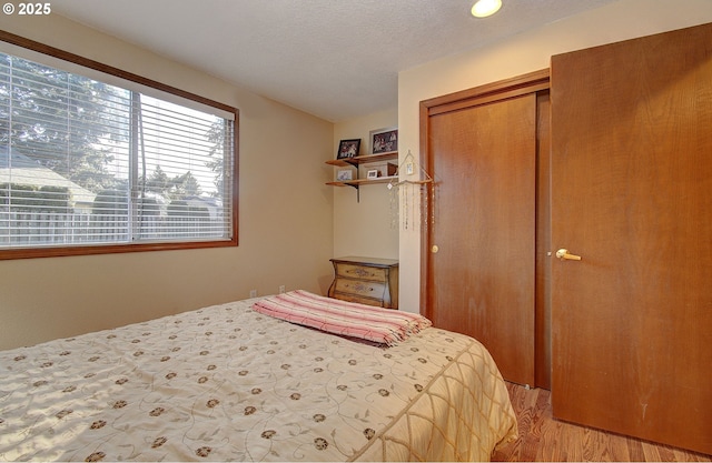 bedroom with a closet, a textured ceiling, and light wood-type flooring