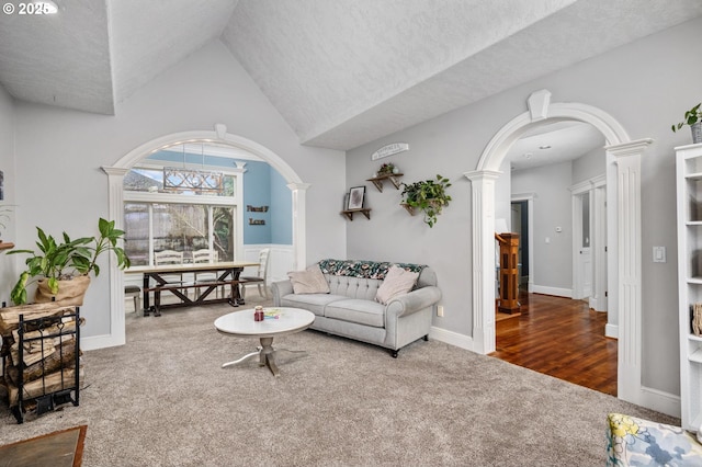carpeted living area featuring arched walkways, decorative columns, and high vaulted ceiling