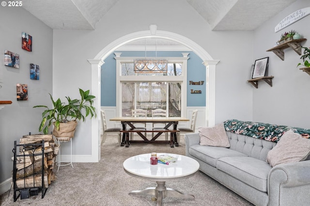 carpeted living area featuring arched walkways, decorative columns, a wainscoted wall, and a chandelier