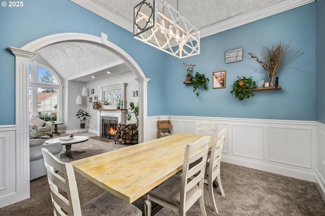 dining area featuring a textured ceiling, arched walkways, wainscoting, carpet flooring, and a tile fireplace