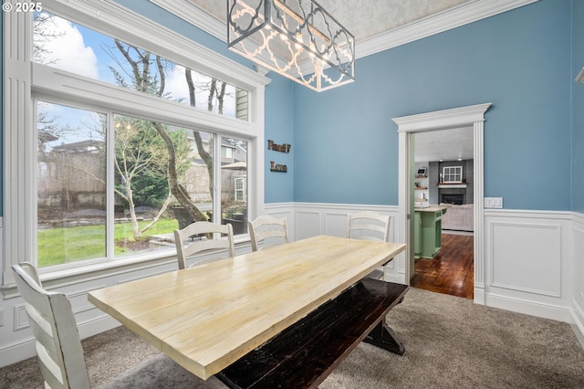 dining room featuring crown molding, carpet floors, a fireplace, an inviting chandelier, and a decorative wall