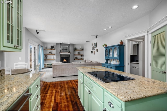 kitchen featuring green cabinetry, dark wood-type flooring, a brick fireplace, black electric cooktop, and a center island