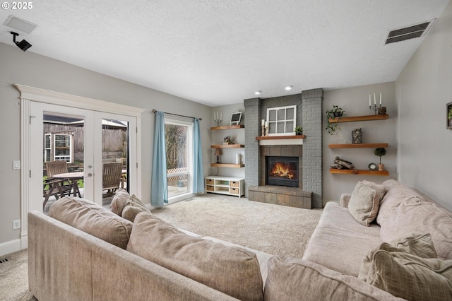 carpeted living room with visible vents, a brick fireplace, baseboards, french doors, and a textured ceiling