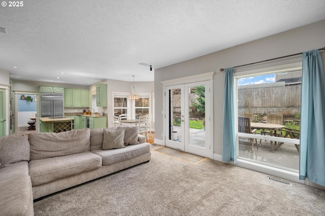 living area featuring a textured ceiling, french doors, visible vents, and light carpet