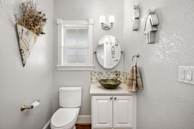 half bathroom with baseboards, toilet, and vanity