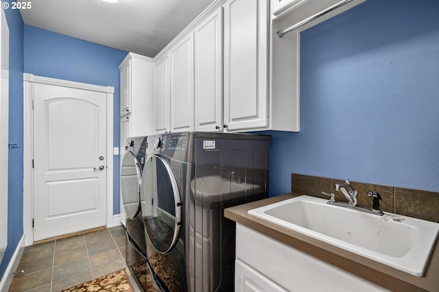laundry area featuring a textured ceiling, independent washer and dryer, cabinet space, a sink, and baseboards