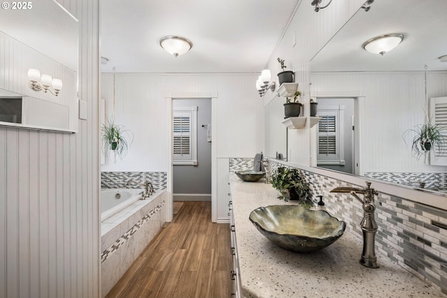 full bath featuring backsplash, a garden tub, wood finished floors, and vanity