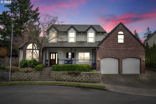 traditional home featuring roof with shingles, brick siding, a garage, covered porch, and driveway
