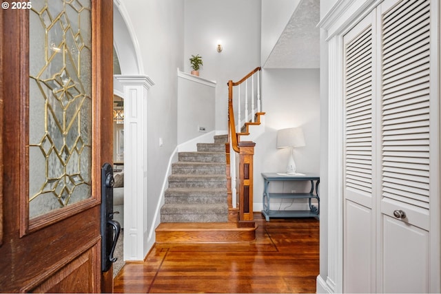 entryway with stairway, wood finished floors, baseboards, decorative columns, and arched walkways