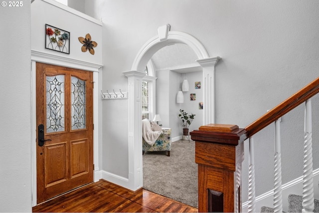 entrance foyer with dark wood-style floors, baseboards, ornate columns, arched walkways, and stairs