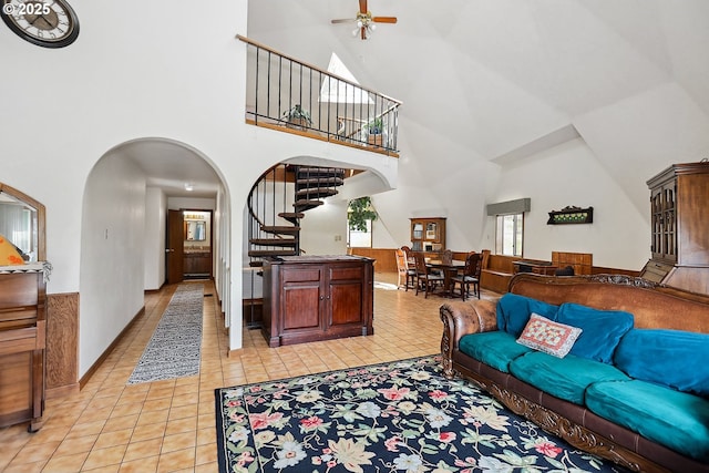 living room featuring light tile patterned flooring, ceiling fan, a towering ceiling, stairway, and arched walkways