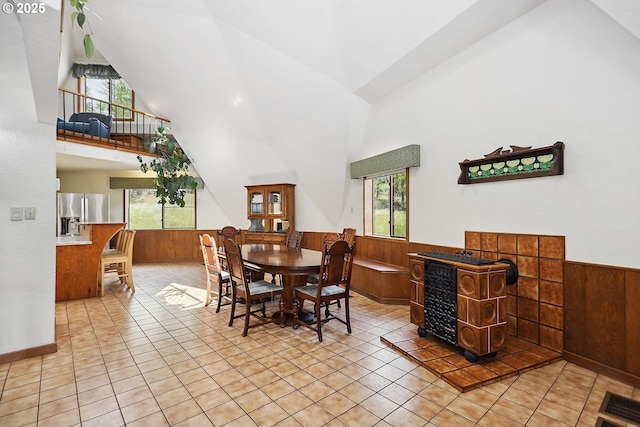 dining room with light tile patterned flooring, high vaulted ceiling, wooden walls, and wainscoting