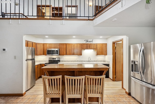kitchen with light tile patterned floors, a center island, a towering ceiling, appliances with stainless steel finishes, and brown cabinets