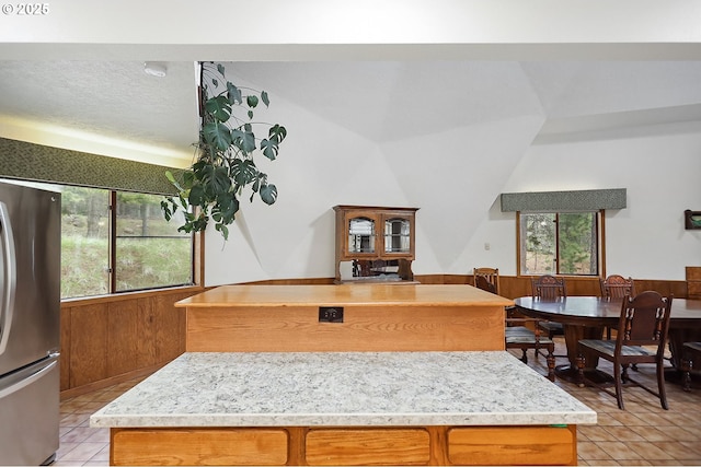 kitchen featuring light countertops, a center island, brown cabinetry, light tile patterned floors, and freestanding refrigerator